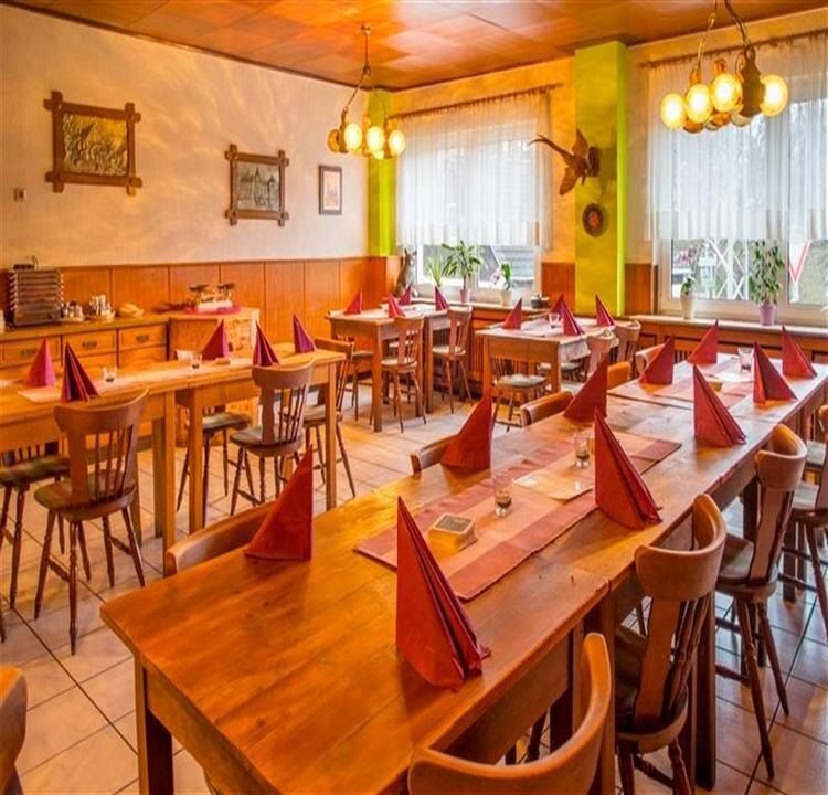 Saal mit langen Holztischen, roten Servietten, Fenstern mit weißen Gardinen und grüner Säule