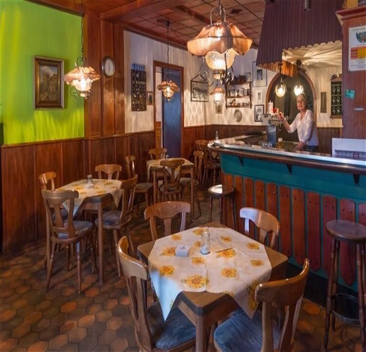 Gaststube mit Holzvertäfelung und grüner Wand, Tische mit gelben Tischdecken, rechts der Tresen mit grünen Holzfeldern